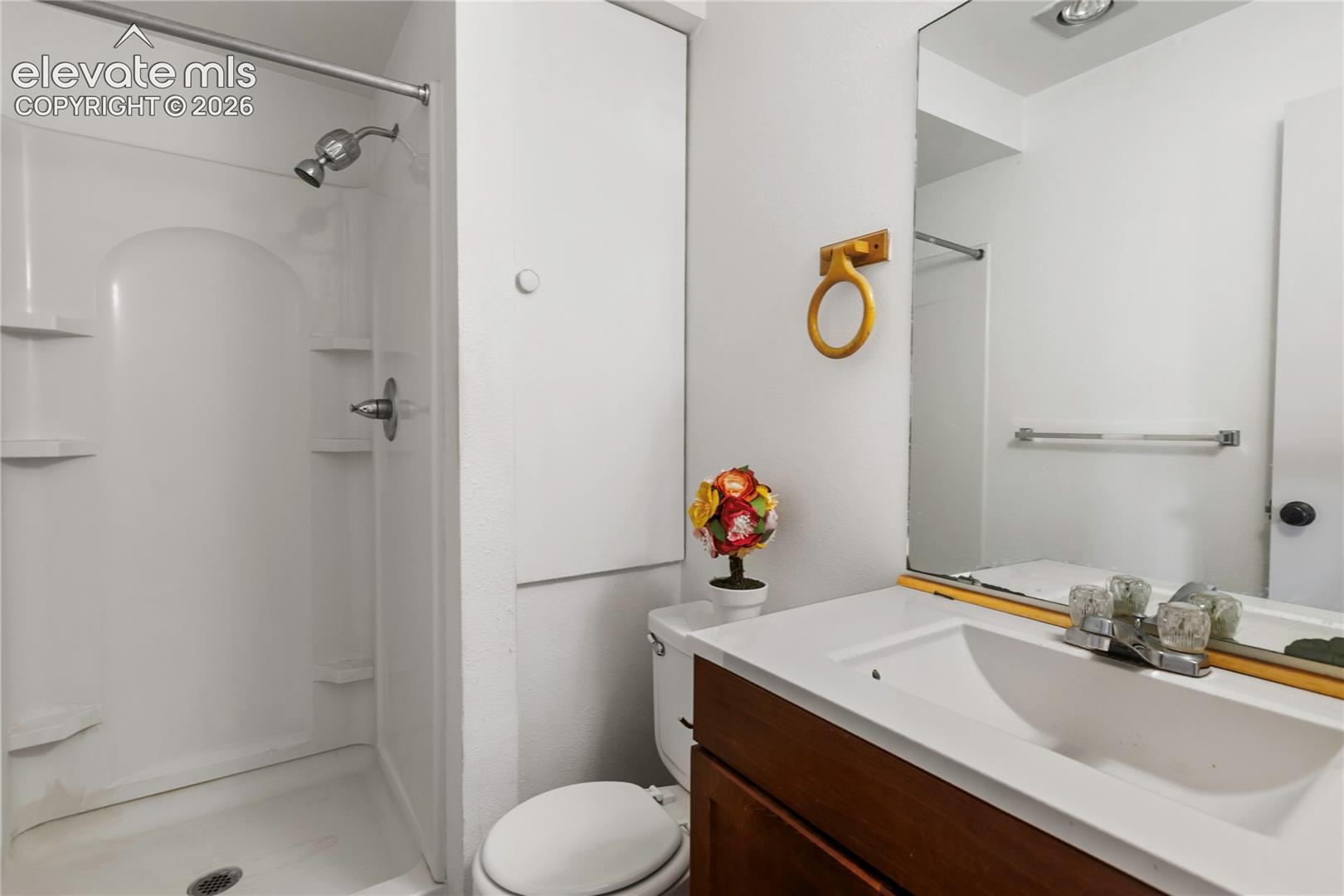 Bathroom featuring a white shower stall with built-in shelving, a wood-finish vanity with an integrated sink, a wall-mounted mirror, and a toilet