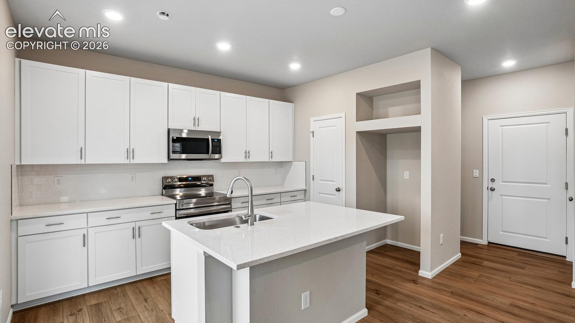 Contemporary kitchen featuring white cabinetry, stainless steel appliances, a center island with sink, quartz countertops, and wood-finish flooring
*photos of a model home*
