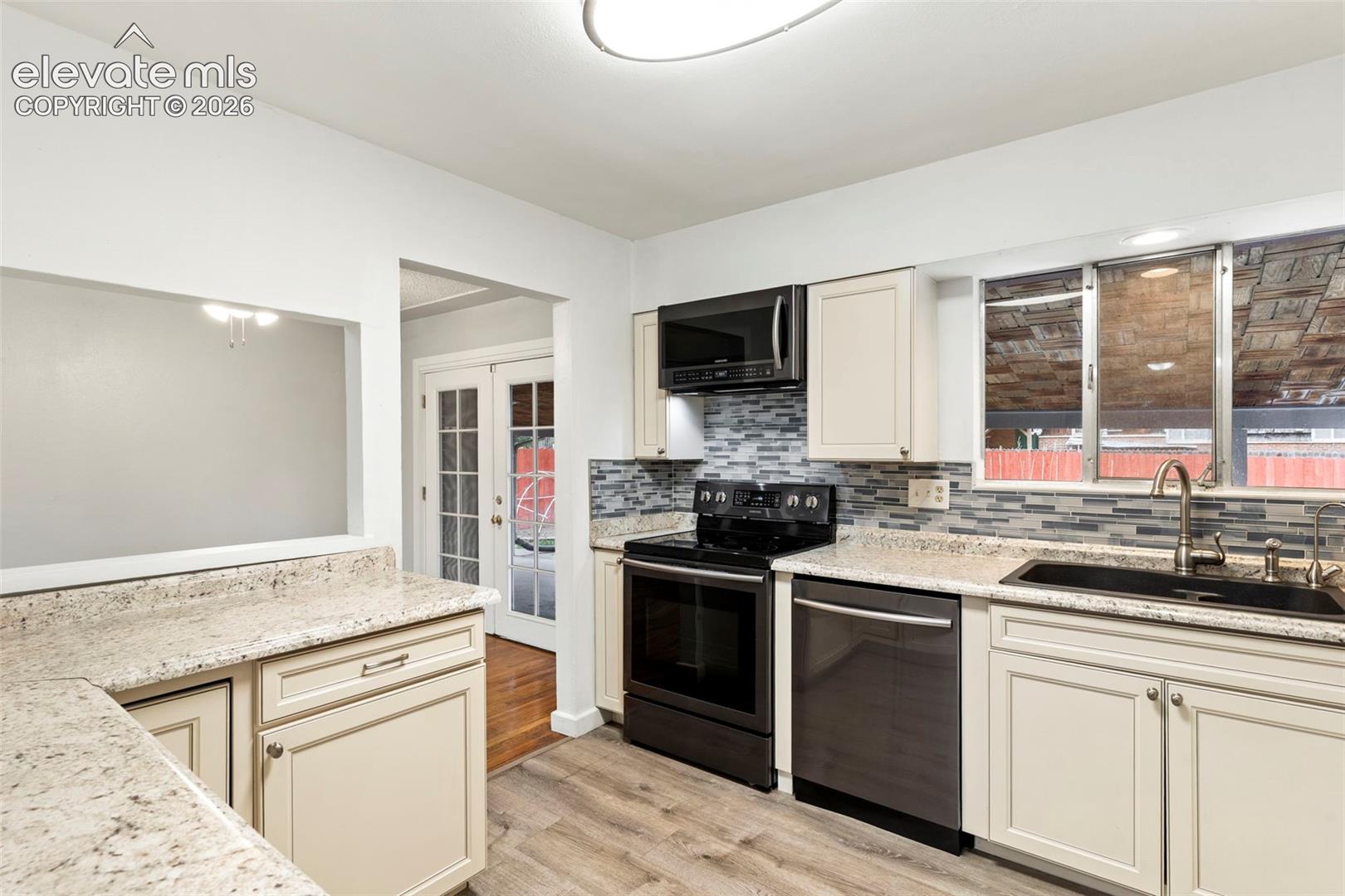 Kitchen featuring light-toned cabinetry, speckled countertops, and a mosaic tile backsplash