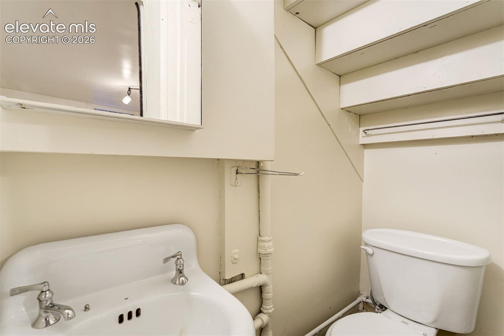 Wall-mounted medicine cabinet with mirror, pedestal sink with dual-handle polished chrome faucet, and standard toilet