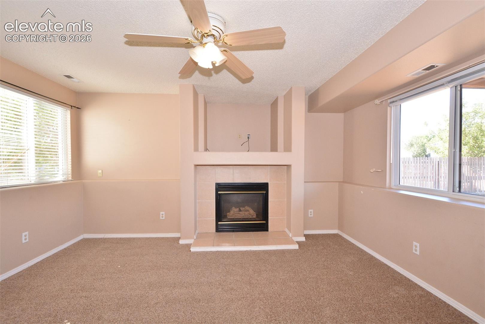 Living area featuring a fireplace with a tile hearth and surround, built-in shelving alcove, neutral carpeting, and a ceiling fan with integrated lighting