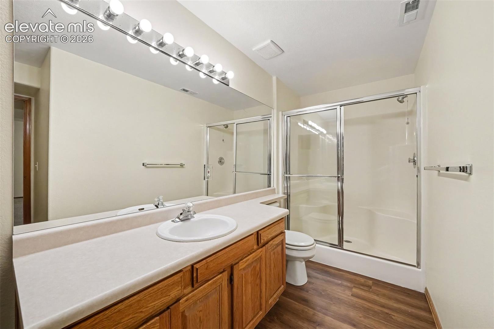 New LVP flooring, full vanity with integrated sink, expansive wall-mounted mirror, and a glass-enclosed shower