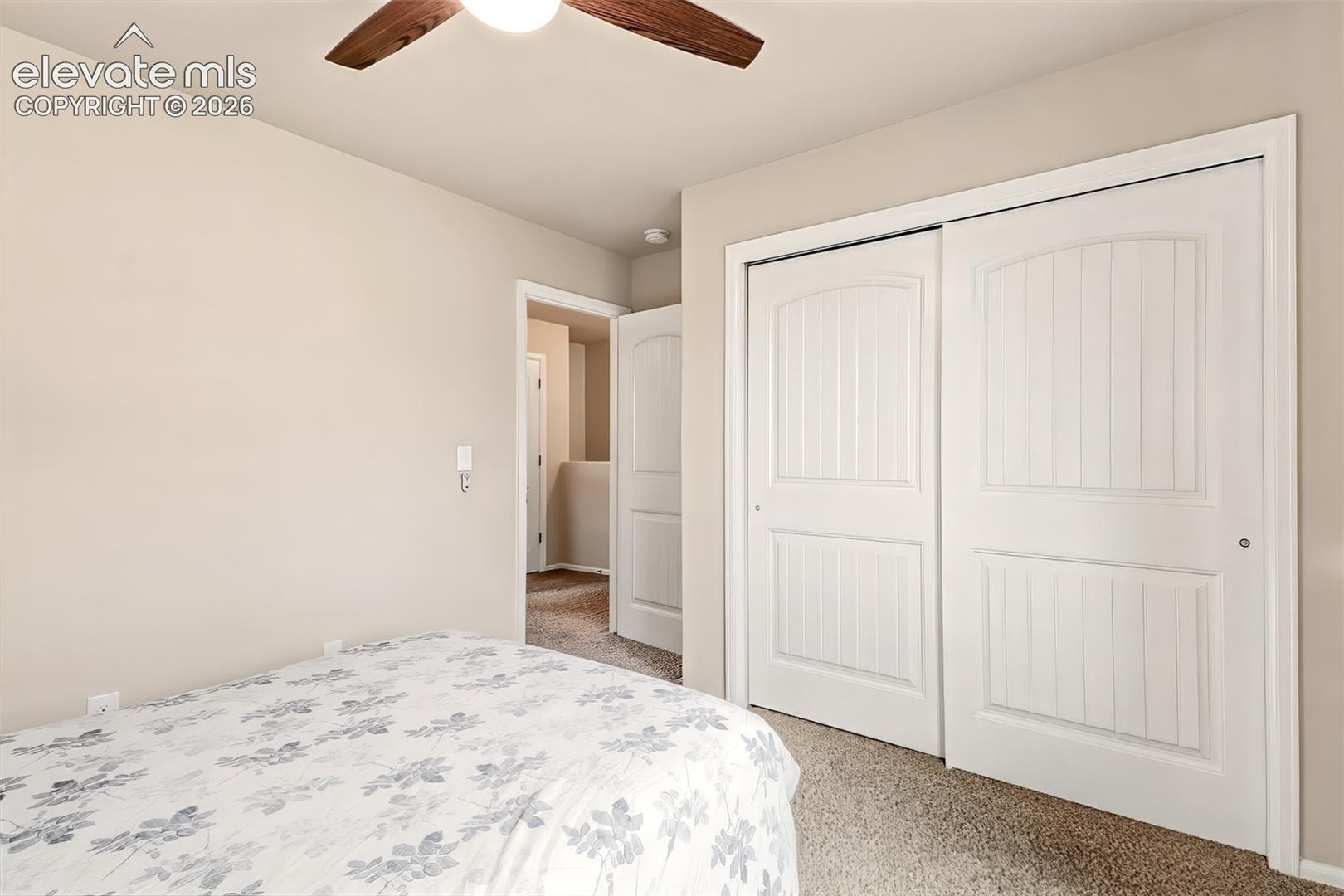 Neutral-toned walls, carpeted flooring, sliding closet doors with vertical panel detailing, and a ceiling fan with light fixture