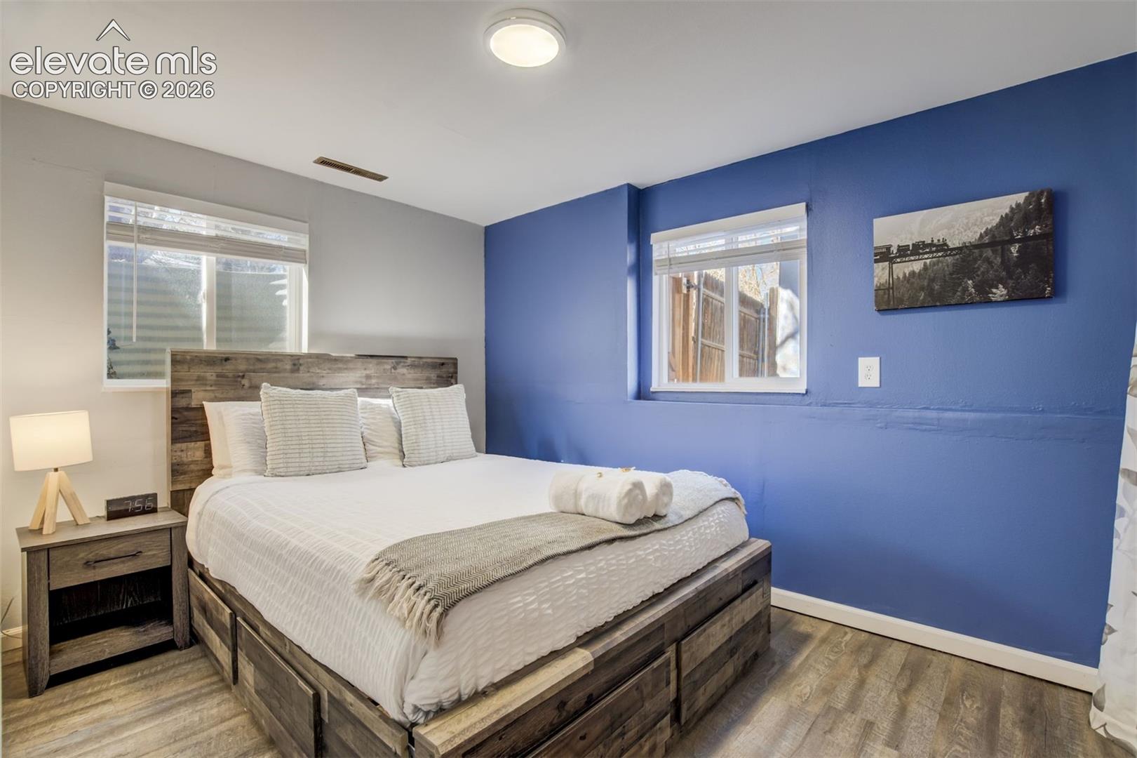 Wood-finish flooring, accent wall, wood-finish bed frame, built-in window, and ceiling-mounted light fixture