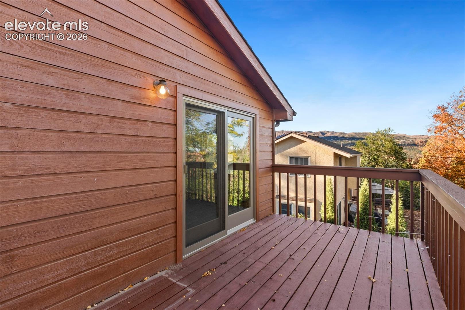 Elevated wooden deck featuring horizontal lap siding, sliding glass doors, integrated wall-mounted lighting, and a slatted railing
