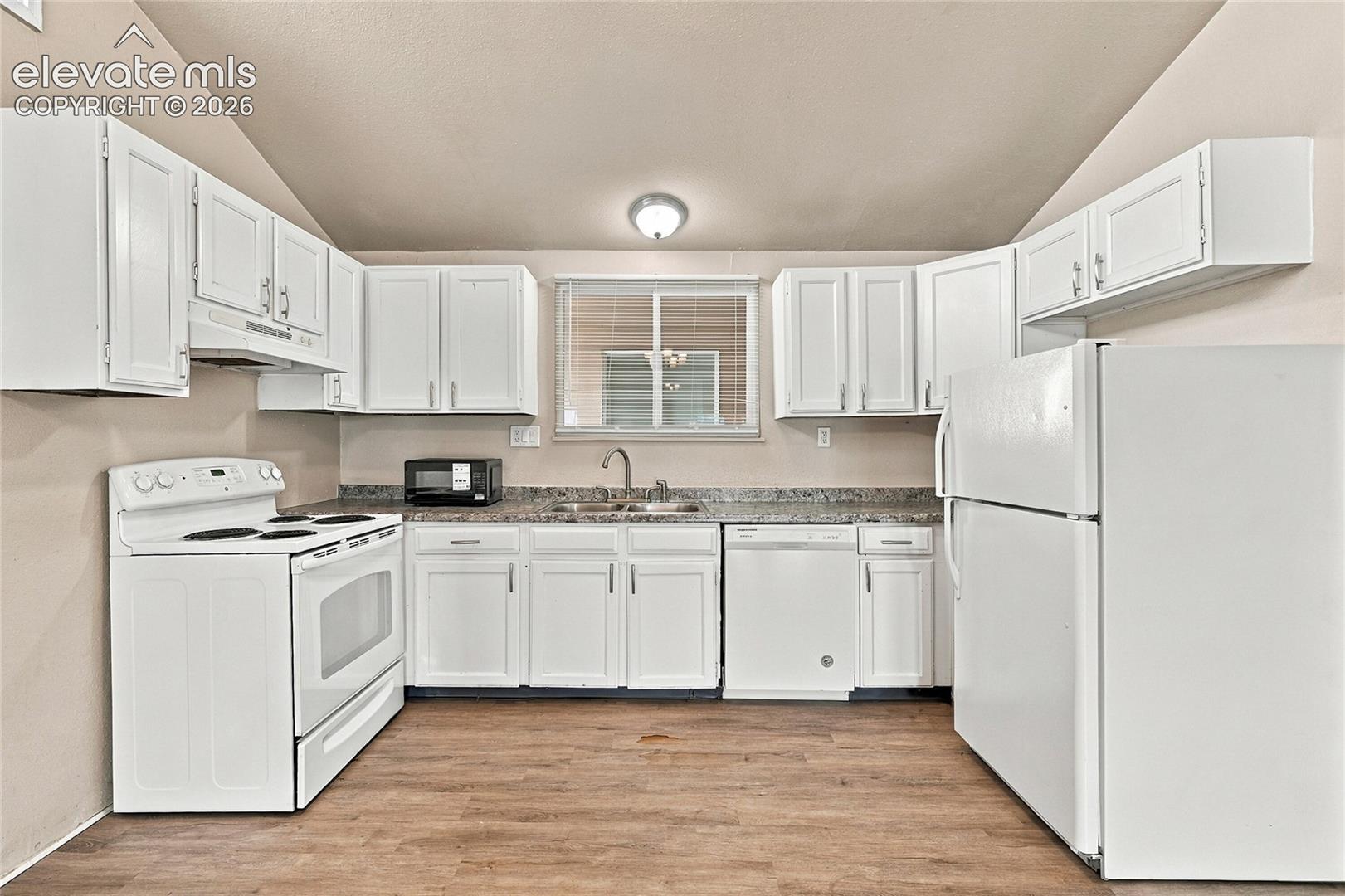 Kitchen featuring white cabinetry, wood-finish flooring, stone-patterned countertops, a dual-basin sink, and white appliances