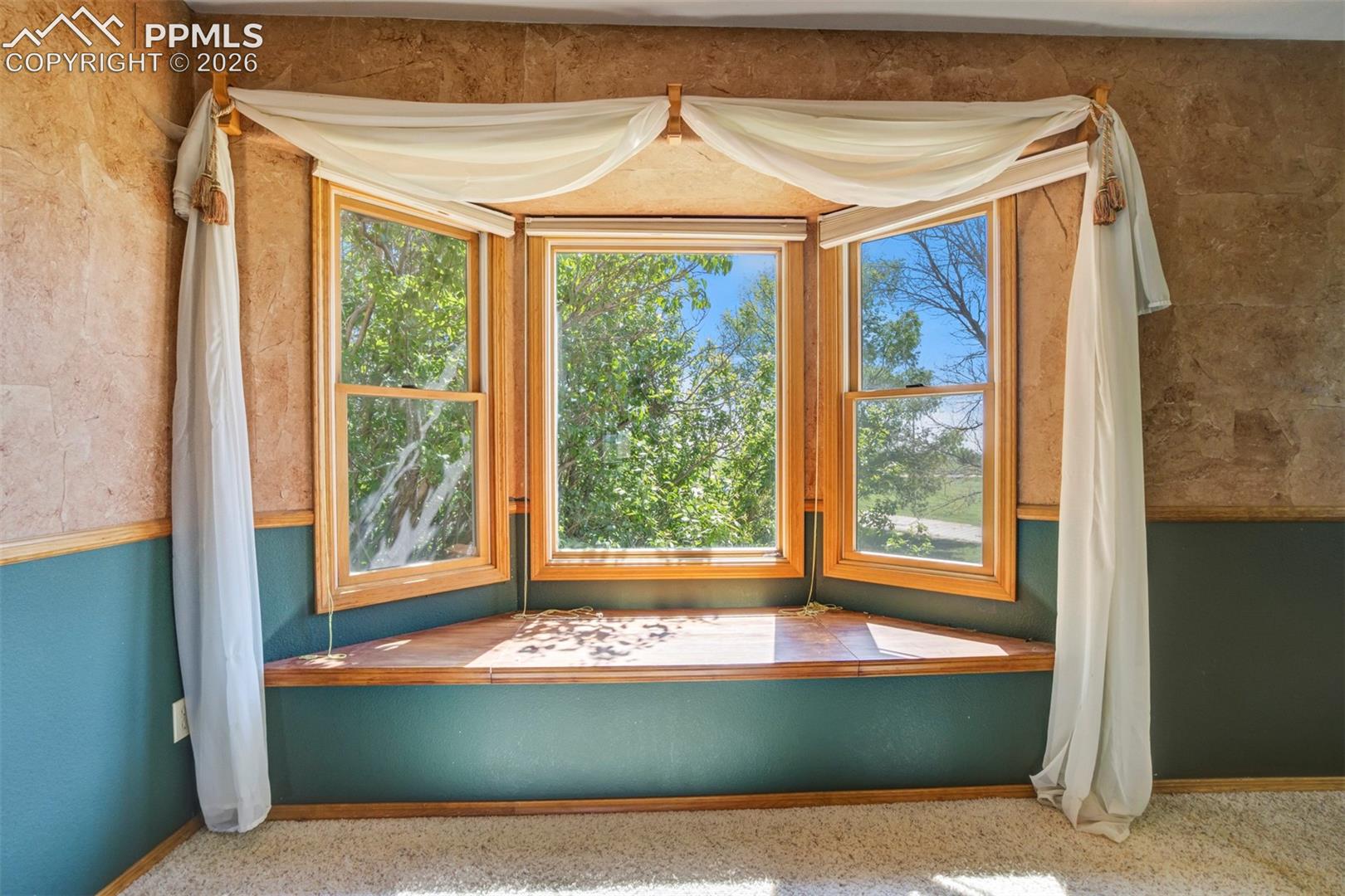 Bay window with natural wood trim, integrated window seat, textured wall finishes, two-tone wall paneling, and soft-toned carpeting