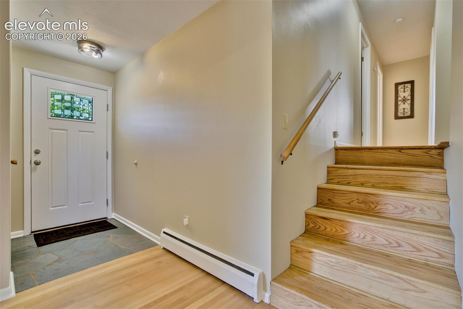 Entryway featuring a white door with a decorative glass insert, slate tile flooring, wood-finish flooring, and a wooden staircase with a wall-mounted handrail