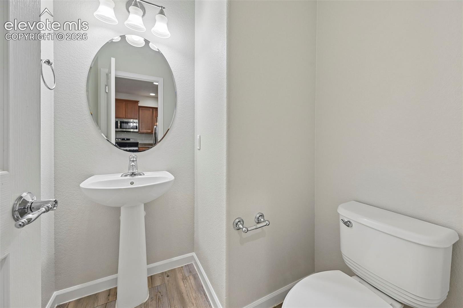Pedestal sink with chrome faucet, oval mirror, and three-bulb vanity light fixture
