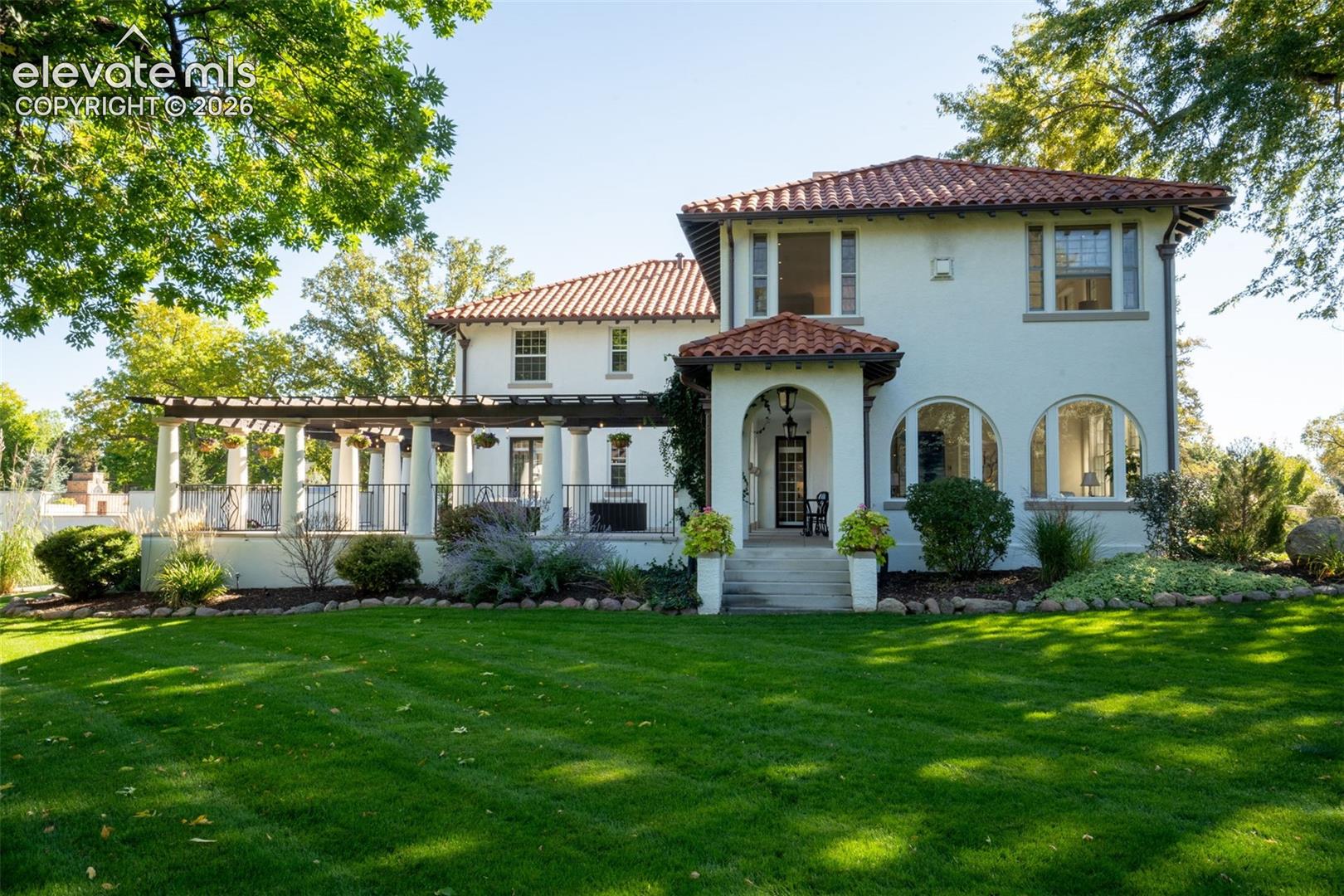 Mediterranean-style residence featuring a red tile roof, arched windows, stucco exterior, a columned pergola, and a covered entry
