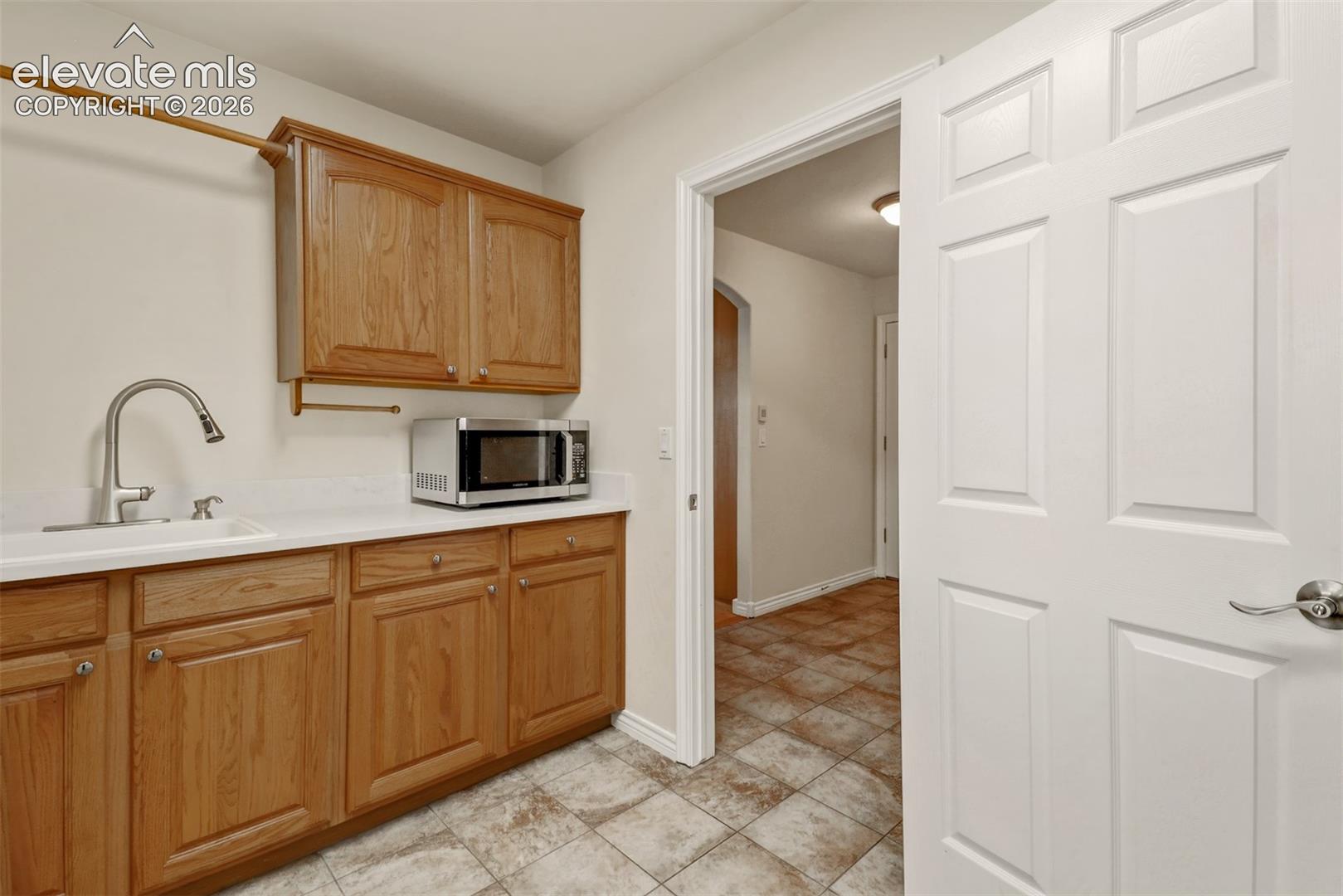 Utility space featuring wood-finish cabinetry, a white countertop, a drop-in sink with a high-arch faucet, and tile flooring