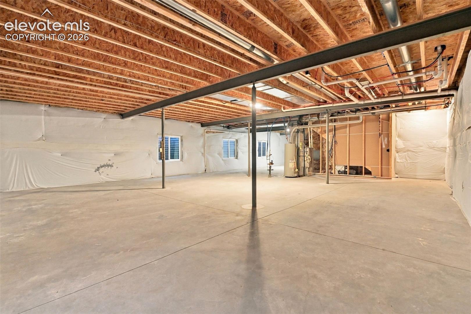 Unfinished lower level featuring an expansive concrete floor, exposed wood joist ceiling, steel support beams, and thermal wall insulation