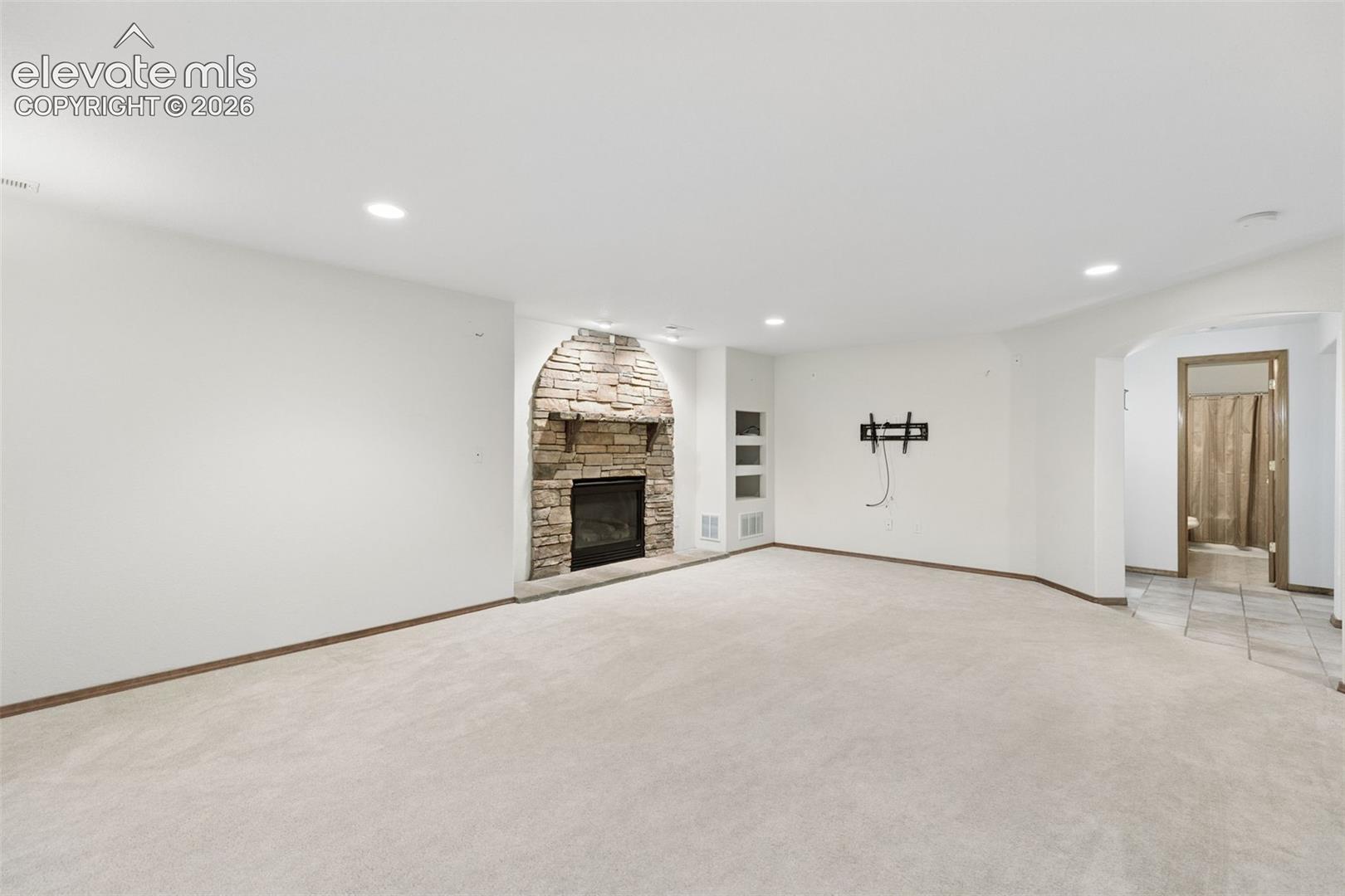 Arched stone fireplace with a wooden mantel, recessed lighting, and wall-mounted shelving niches