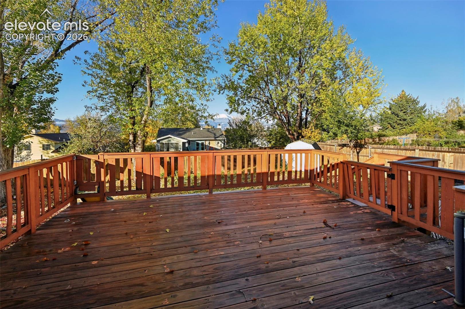 Expansive wood-plank deck featuring perimeter wood railing with gate leading down to yard on one side and sliding board exit on the other side! mature trees, and mountain backdrop