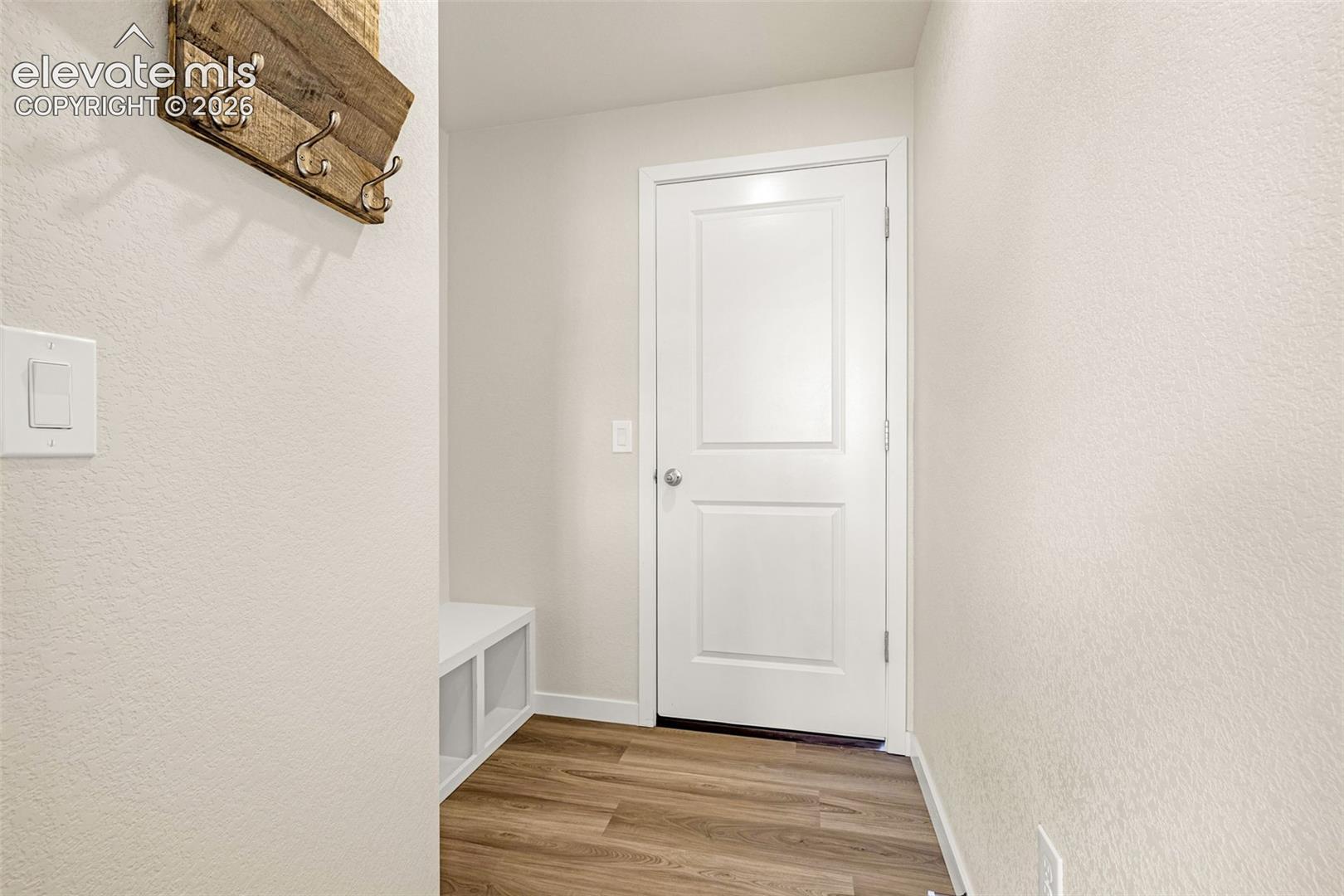 Wood-finish flooring with white trim, featuring a white door and built-in storage bench