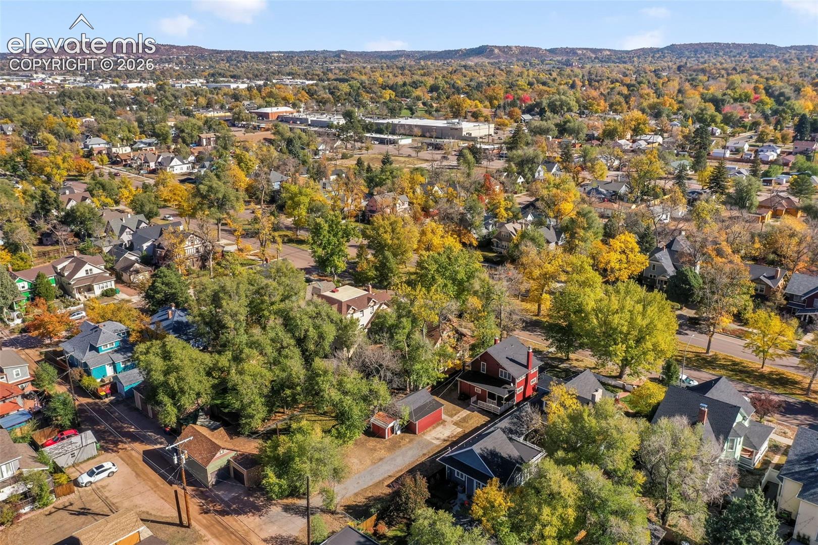 Aerial perspective of a multi-structure property featuring mature tree canopy, expansive lot, and mountain range backdrop
