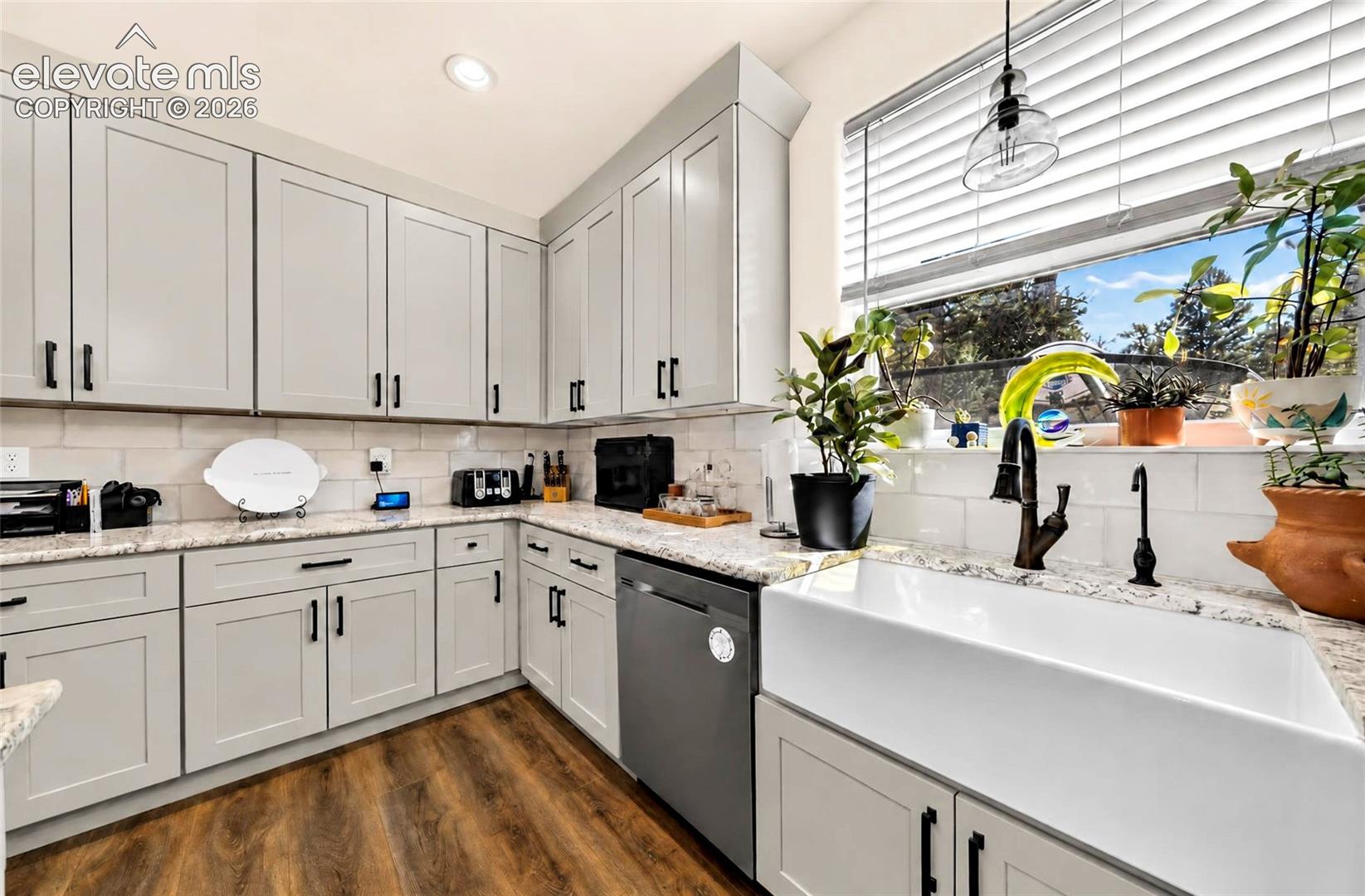 Kitchen featuring light gray shaker cabinetry, light-toned stone-finish countertops, a white farmhouse sink with a high-arch faucet, a white subway tile backsplash, and wood-finish flooring