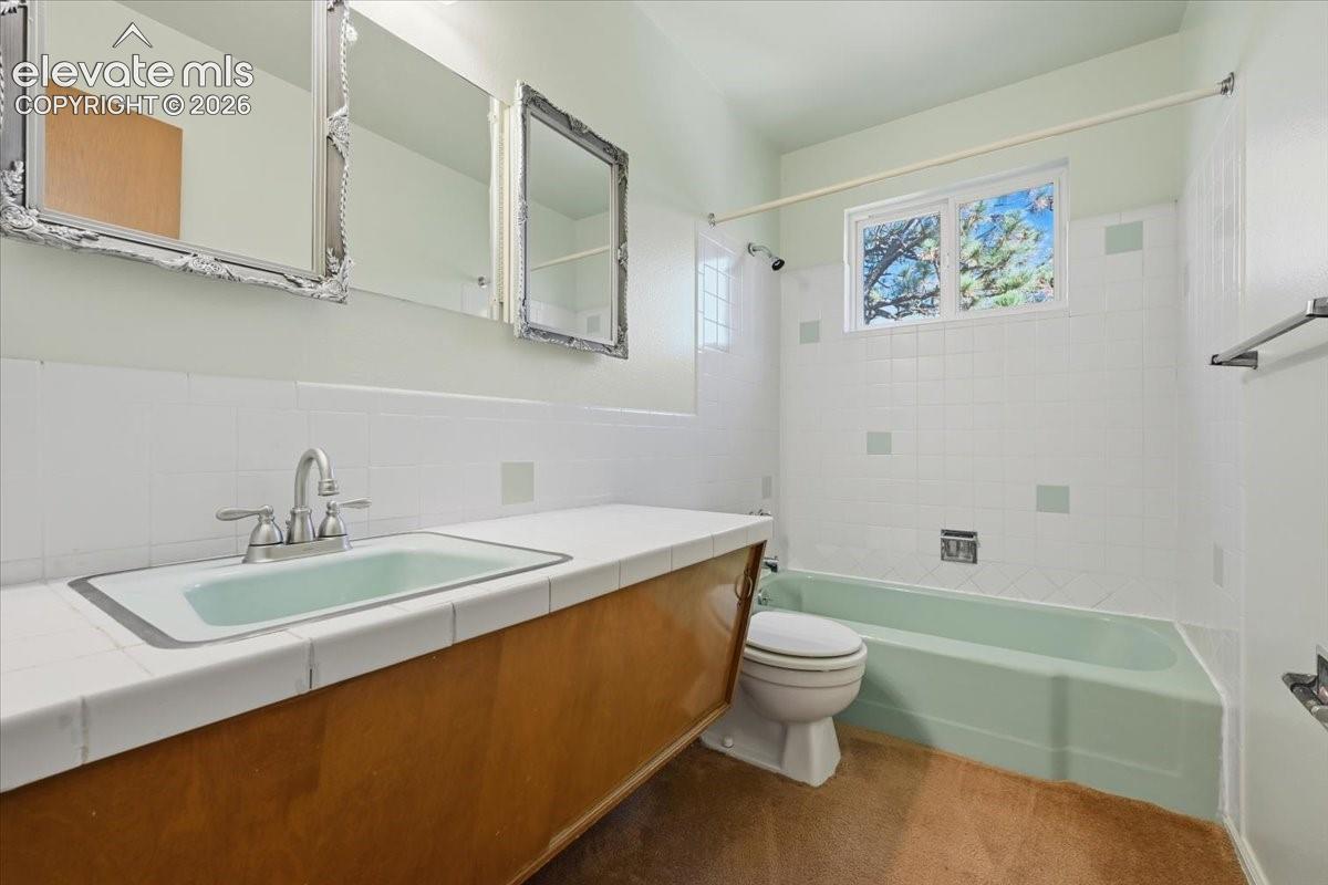 Bathroom featuring a wood-finish vanity with a tile countertop, integrated sink, porcelain bathtub, and tiled wall surround