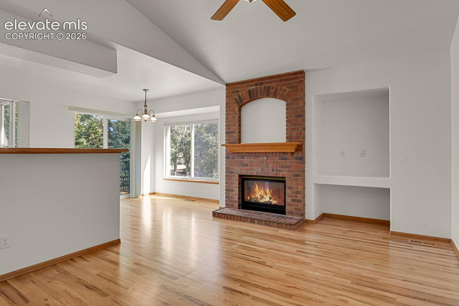 Hardwood flooring throughout, a brick fireplace with a wood mantel, a vaulted ceiling, and built-in shelving