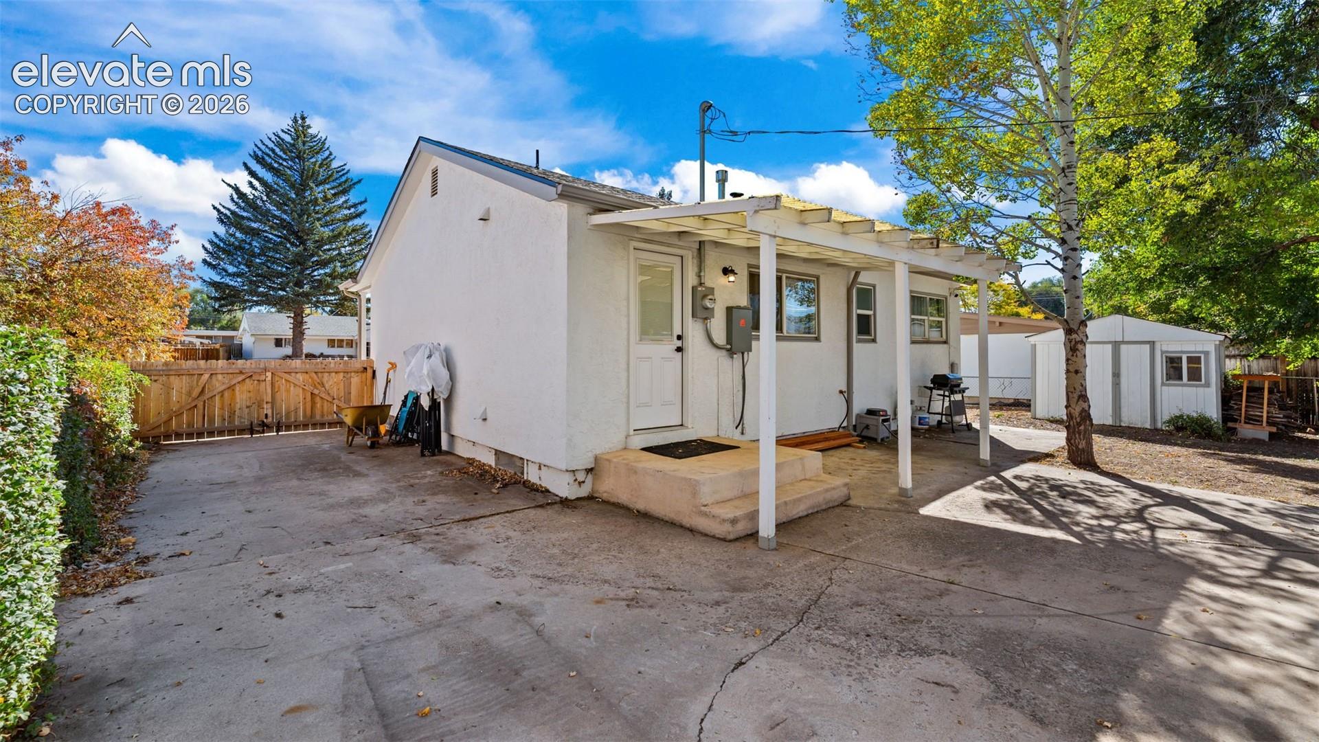 Exterior featuring a concrete driveway, covered patio with a wooden pergola, and a detached storage structure