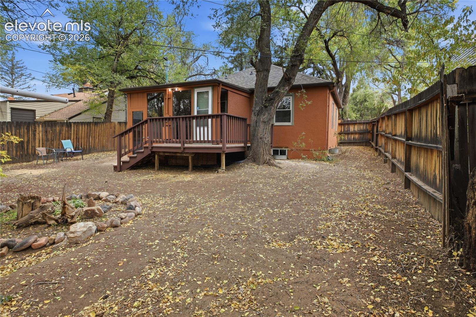 Backyard featuring a raised wooden deck, stone-bordered landscaping, and wood privacy fencing
