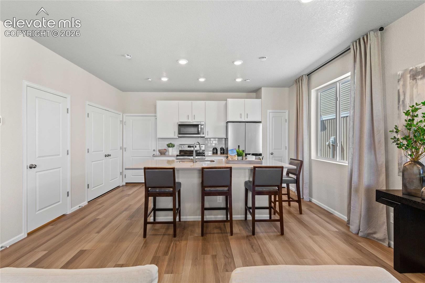 Kitchen featuring white shaker-style 
*photos of a model home*cabinetry, quartz countertops, an expansive center island, stainless steel appliances, and wood-finish flooring
*photos of a model home*