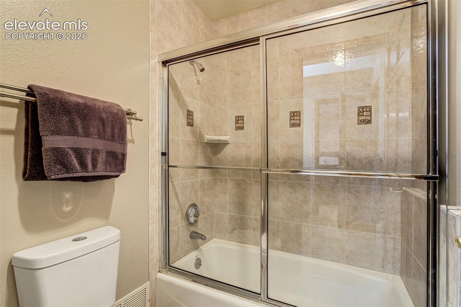 Tub and shower combination with glass sliding doors, tiled surround, and integrated soap dish