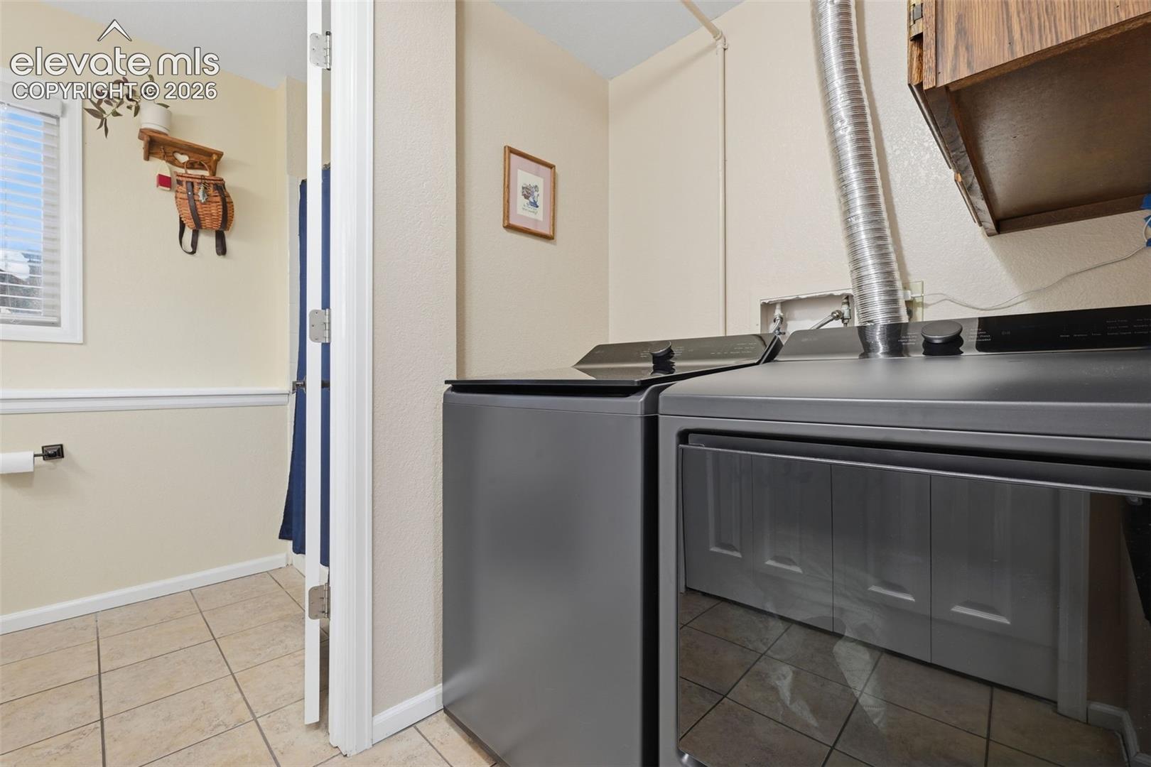 Laundry area featuring tile flooring, white baseboards, and wainscoting