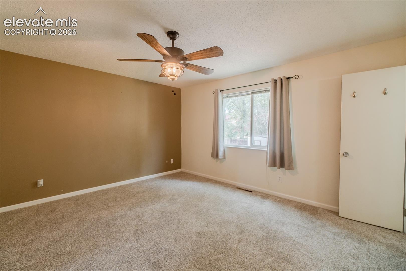 Ceiling fan with integrated lighting, window with drapes, neutral tone carpeting, painted walls