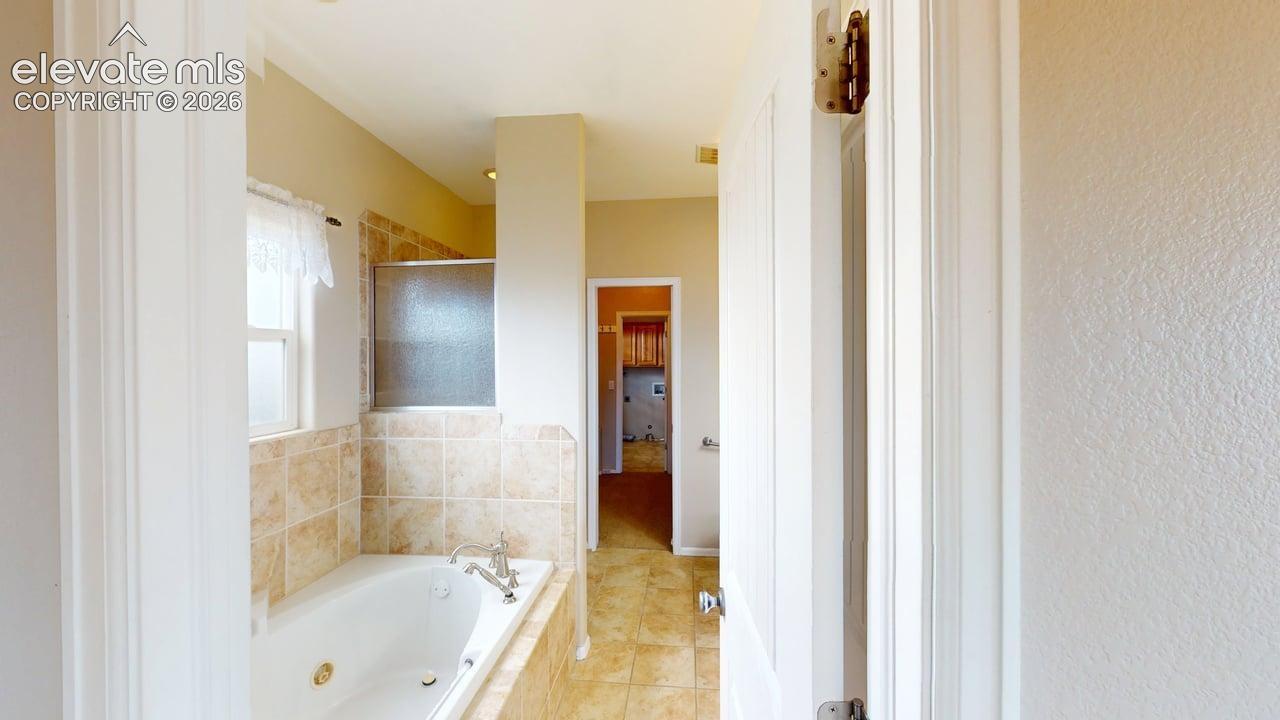Built-in soaking tub with a tiled surround, an integrated shower with a frosted glass enclosure, and tiled flooring