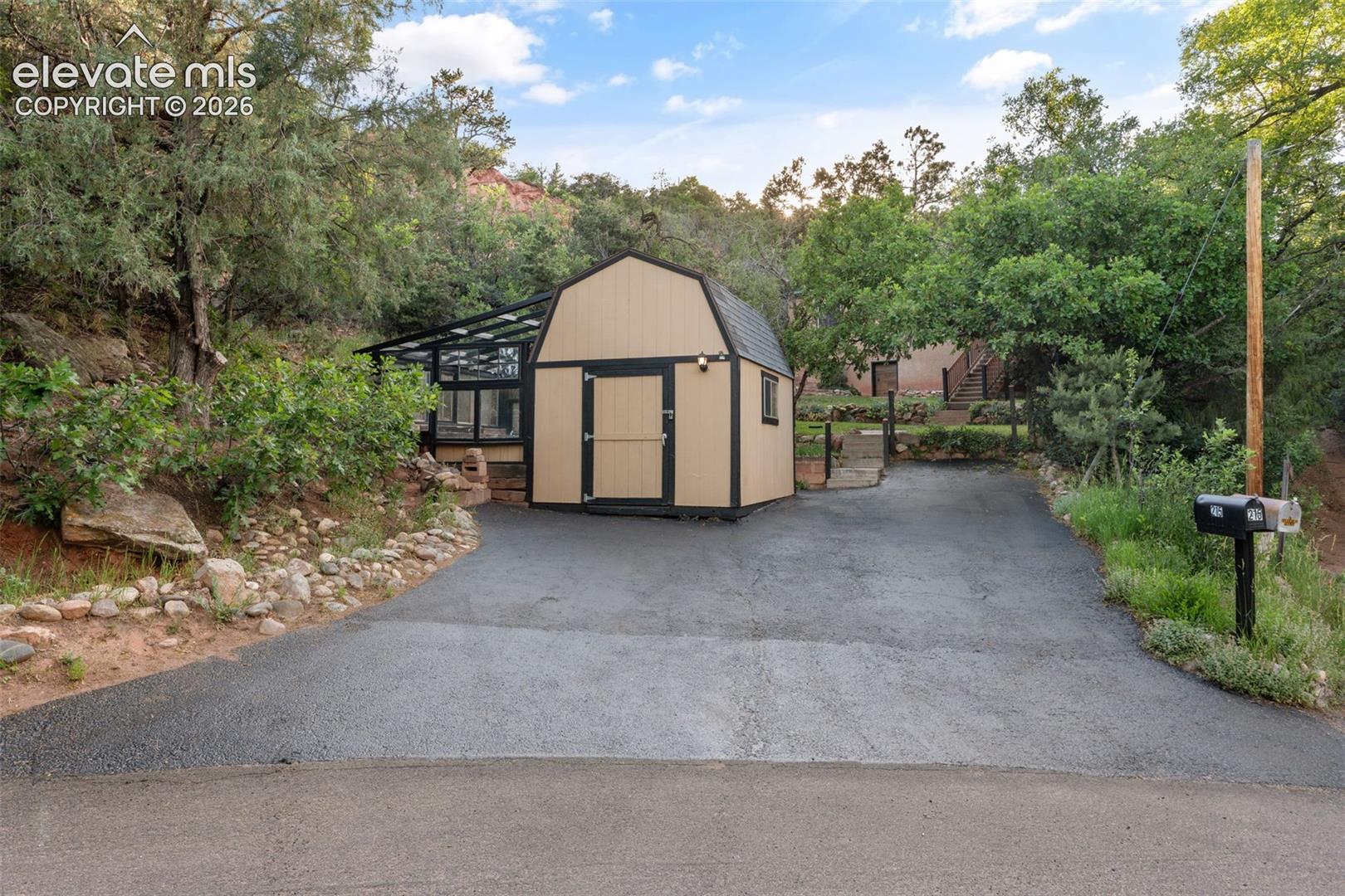 Paved driveway with a detached gambrel-roof structure featuring double entry doors and an attached glass-enclosed space