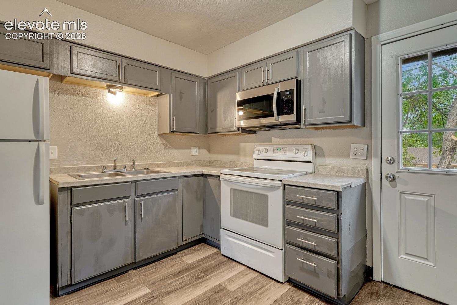Kitchen featuring wood-finish flooring, gray cabinetry with modern hardware, double basin sink, white range, and a stainless steel microwave