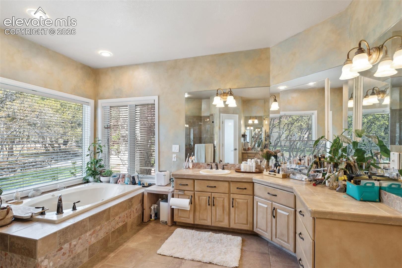 Alcove soaking tub with tile surround, dual vanities with integrated sinks, and expansive mirror array