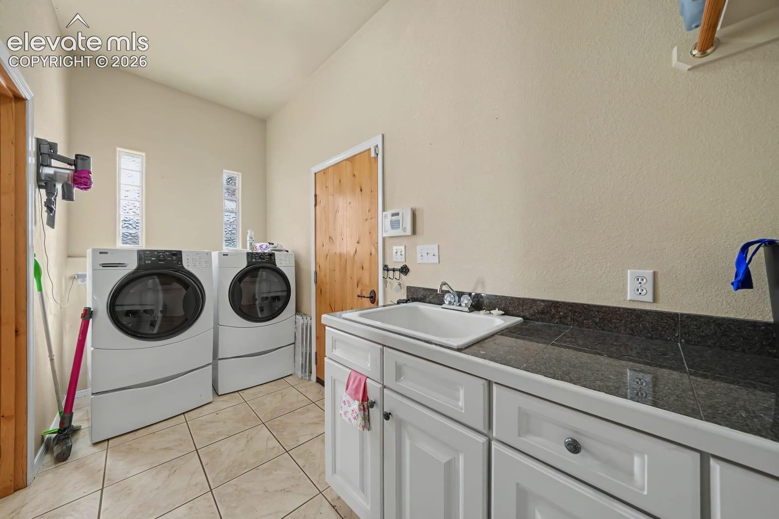 Utility room featuring ceramic tile flooring, custom white cabinetry, a dark stone countertop, a drop-in basin sink with a dual-handle chrome faucet, and dual vertical windows