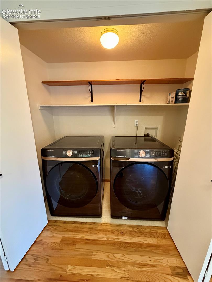 Dedicated laundry area featuring wood-finish flooring, overhead lighting, and built-in shelving
