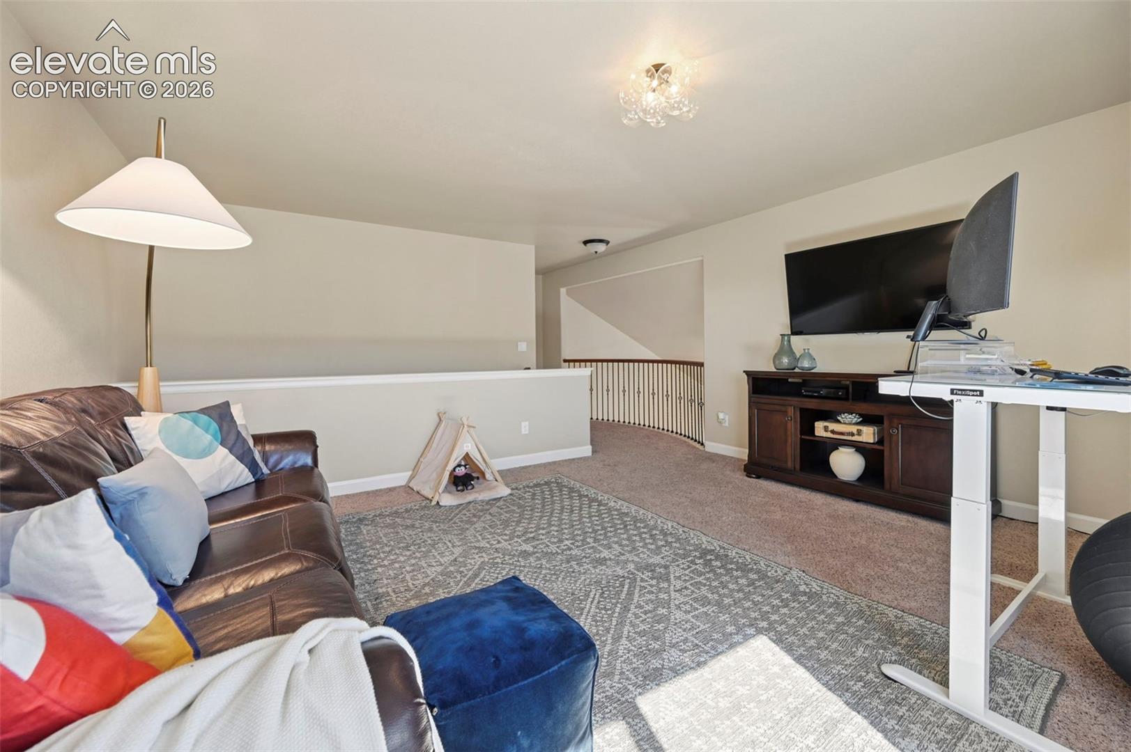 Open-concept loft featuring carpeted flooring and metal railing overlooking the area below