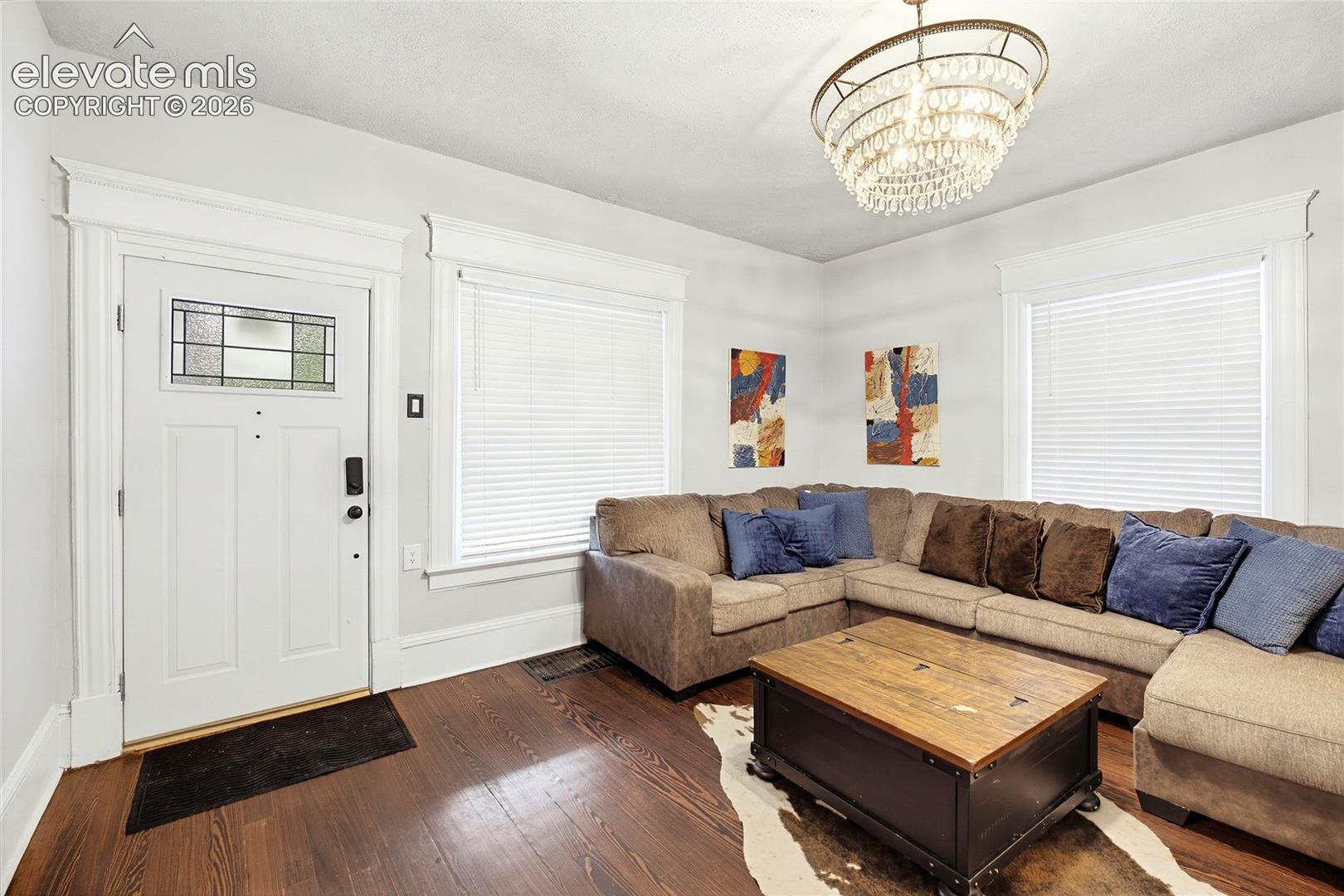 Rich wood-finish flooring, a white paneled entry door with leaded glass, and an ornate crystal chandelier