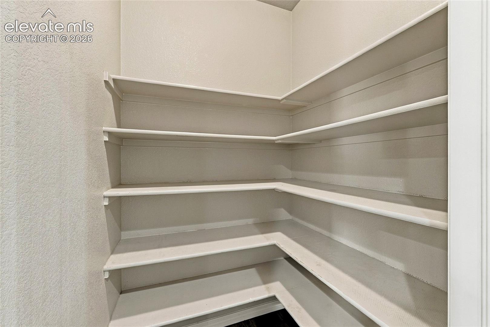 Storage area featuring five tiers of custom built-in white shelving and neutral wall finishes
