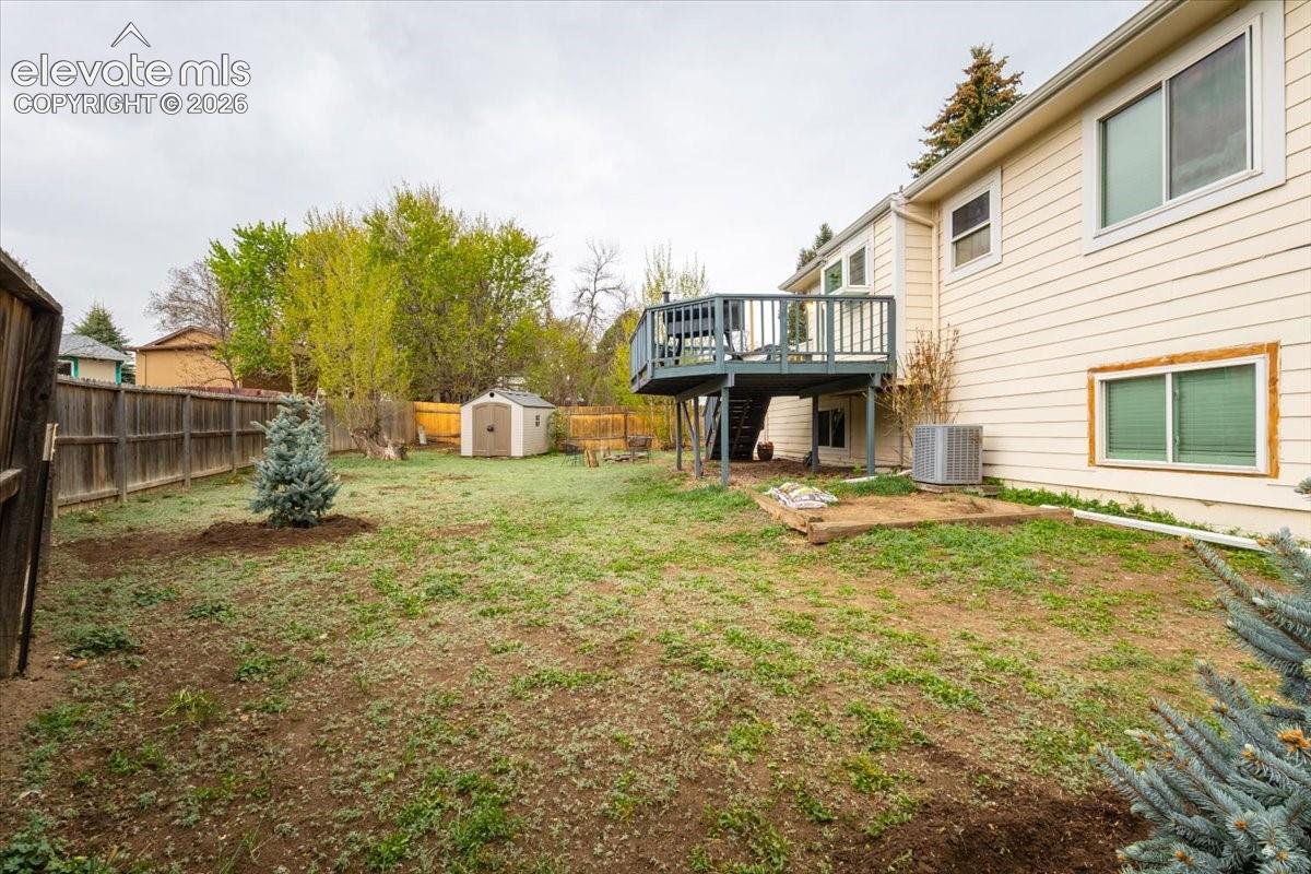 Expansive backyard featuring a fenced perimeter, a rear deck with stairs, a storage shed, and mature trees