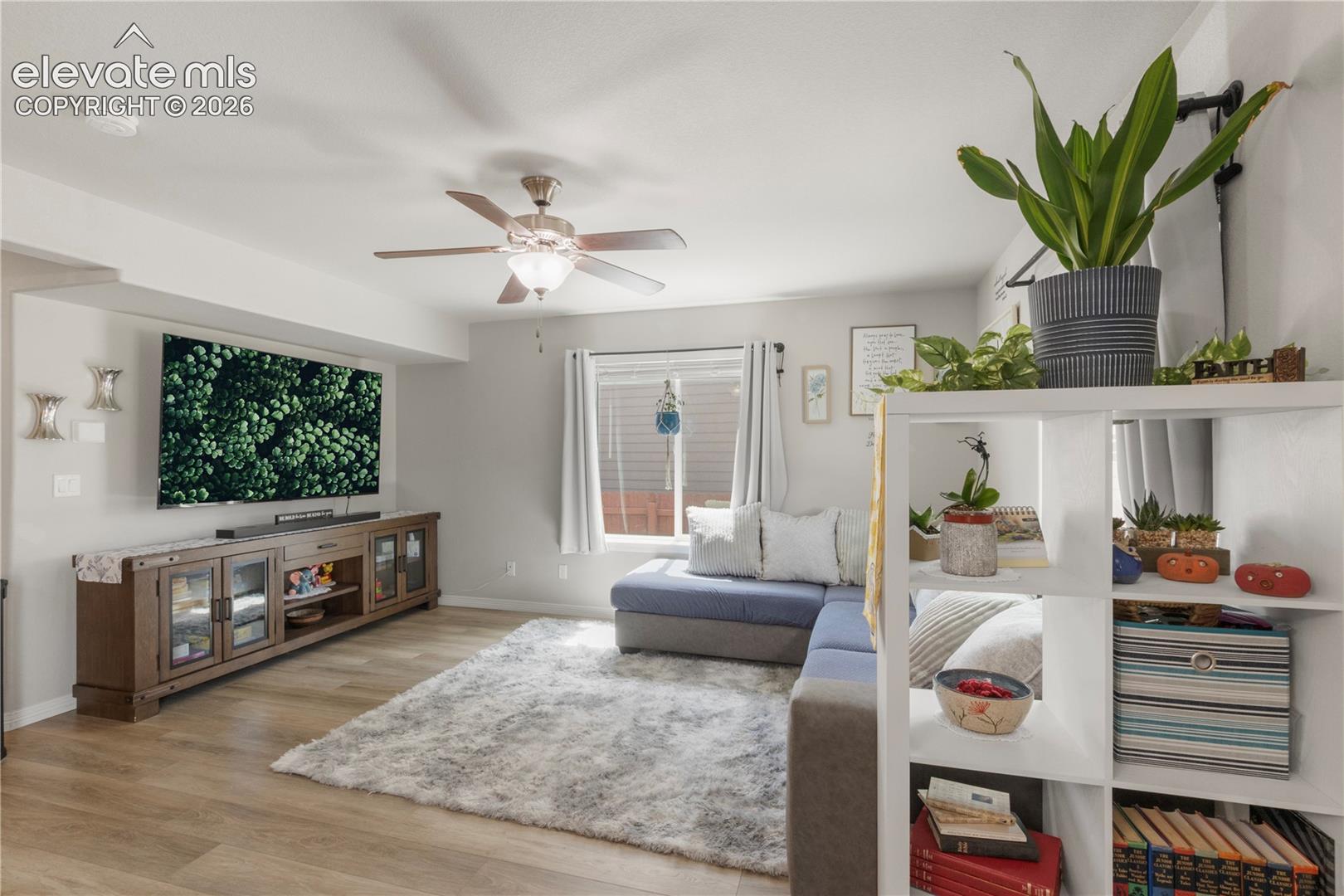Wood-finish flooring, ceiling fan with integrated lighting, recessed lighting, wall-mounted television, and a built-in media console