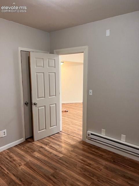 Neutral-toned walls, wood-finish flooring, six-panel interior door, and metallic baseboard heating unit