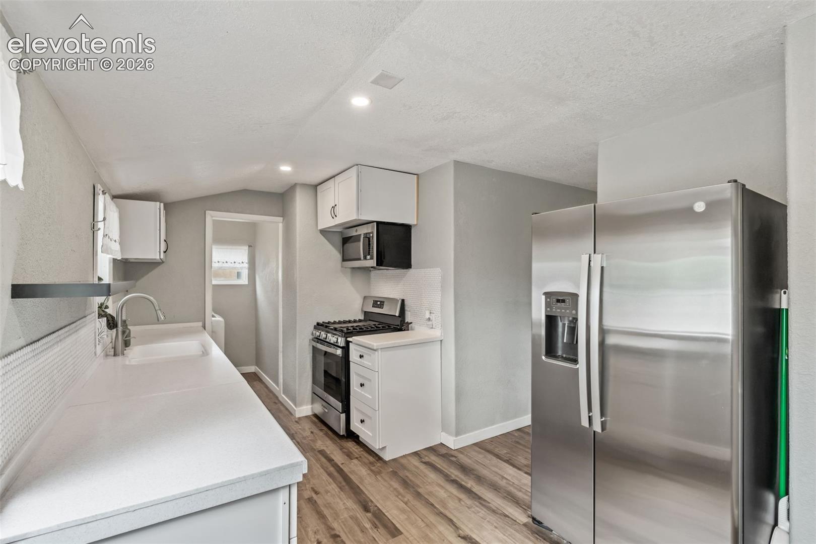 Kitchen featuring white cabinetry, light countertops, wood-finish flooring, stainless steel appliances, and a tiled backsplash