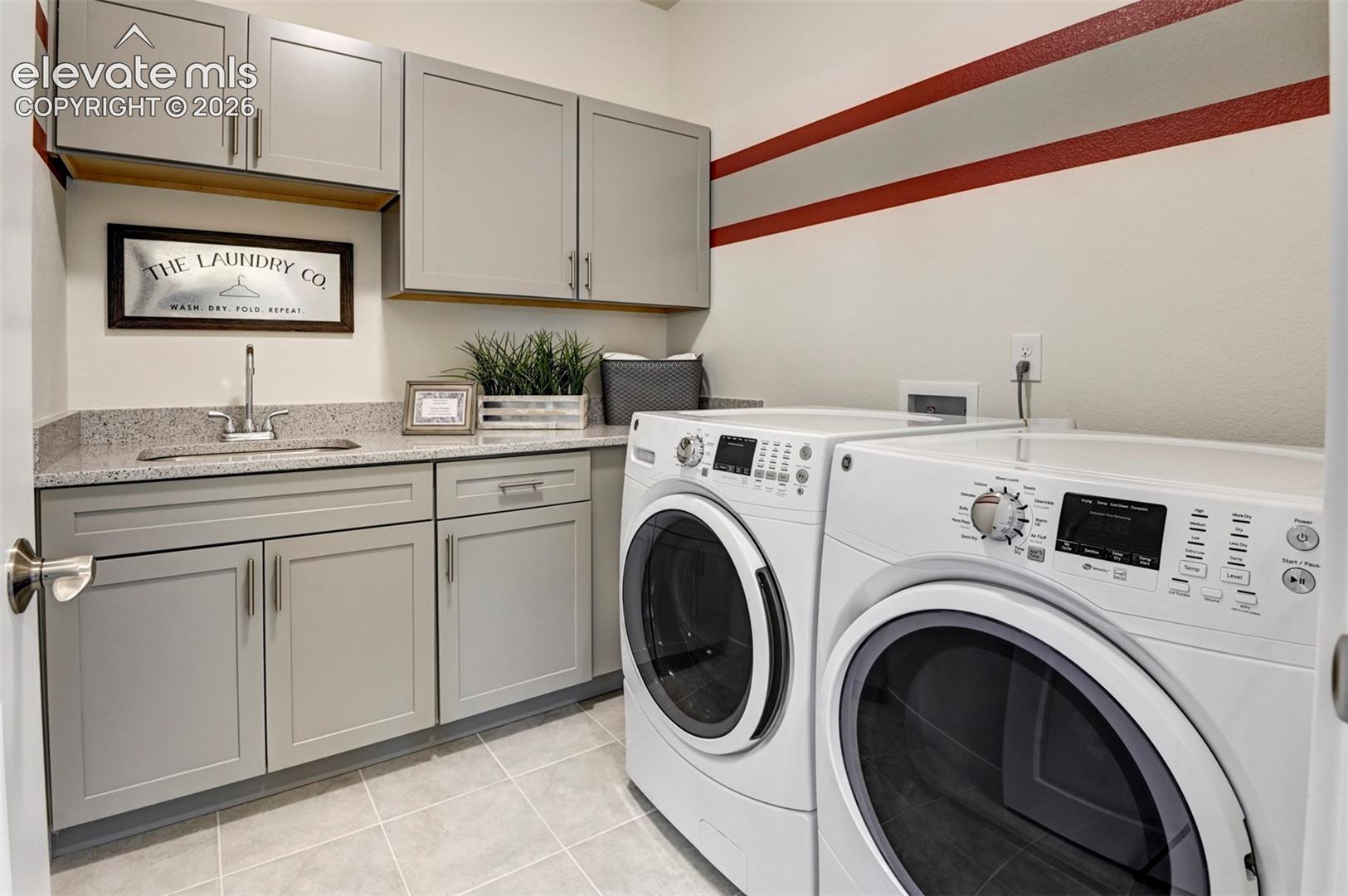 Laundry area with light gray cabinetry, granite-finish countertop, and a built-in sink with a stainless steel faucet