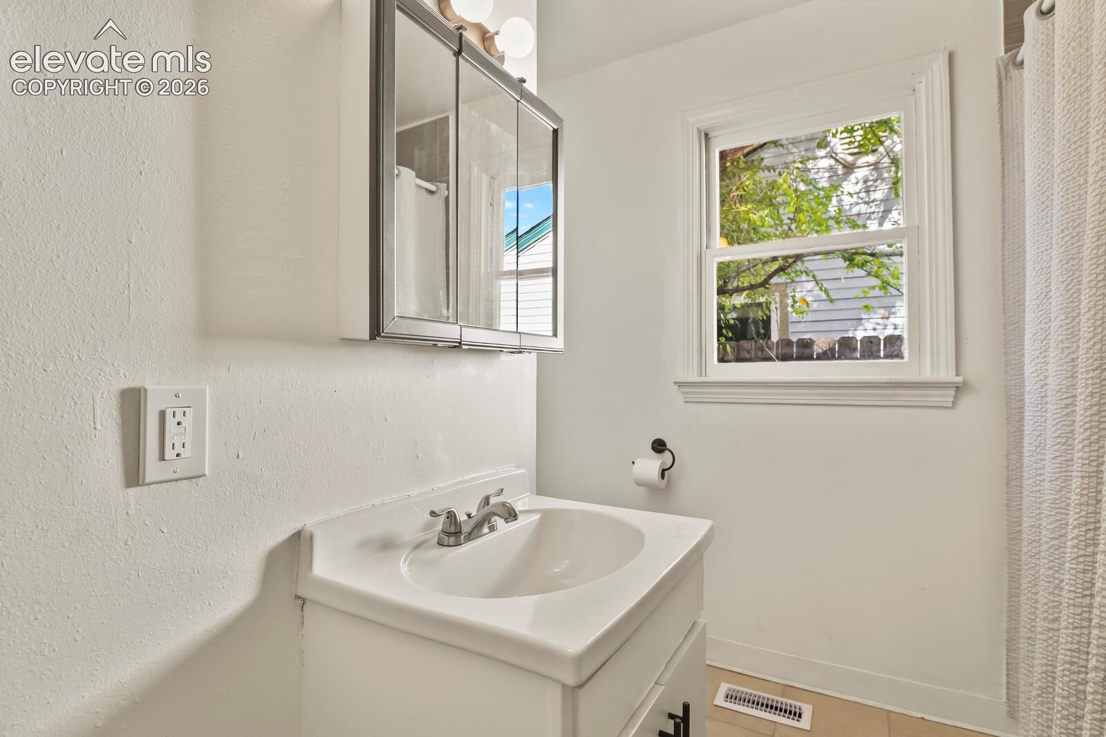 White vanity with integrated sink, medicine cabinet, tile flooring and cast iron tub