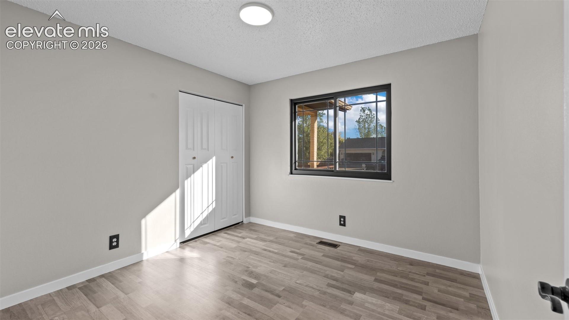 Bright, light-filled room featuring wood-finish flooring, recessed ceiling lighting, and a large window with black-framed glass panes offering natural illumination