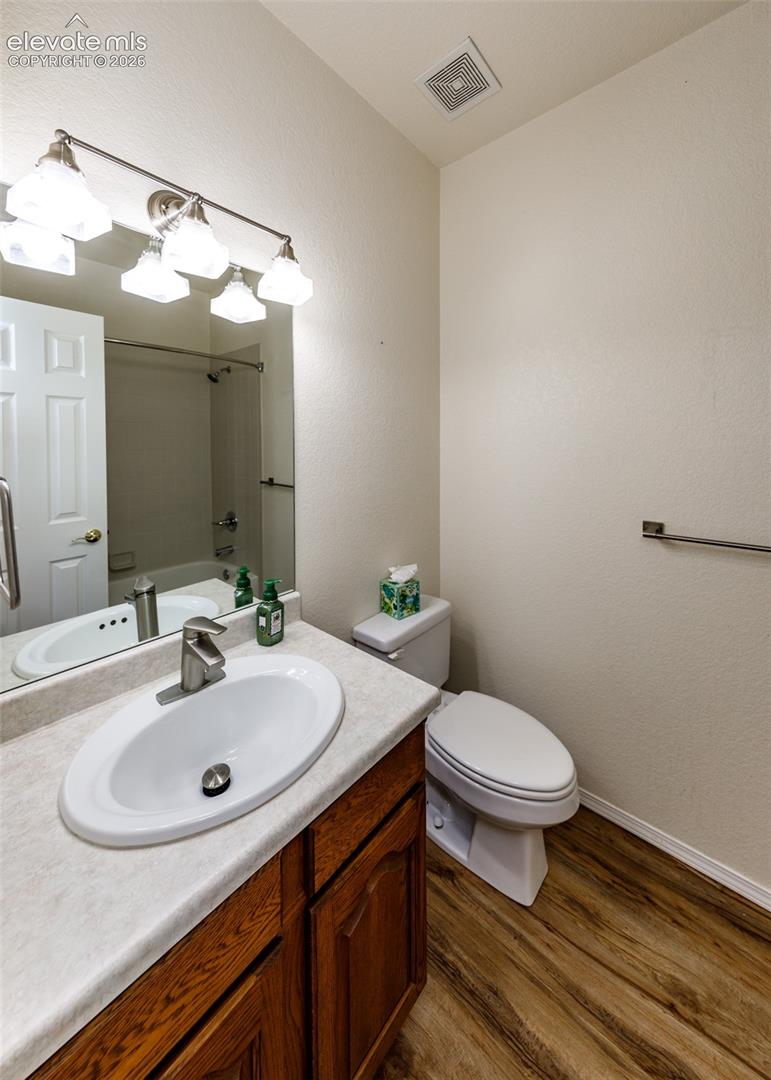 Bedroom #2 Bathroom featuring wood-finish flooring, a vanity with a solid-surface countertop and integrated oval sink, a multi-bulb vanity light fixture, and an oversized wall-mounted mirror