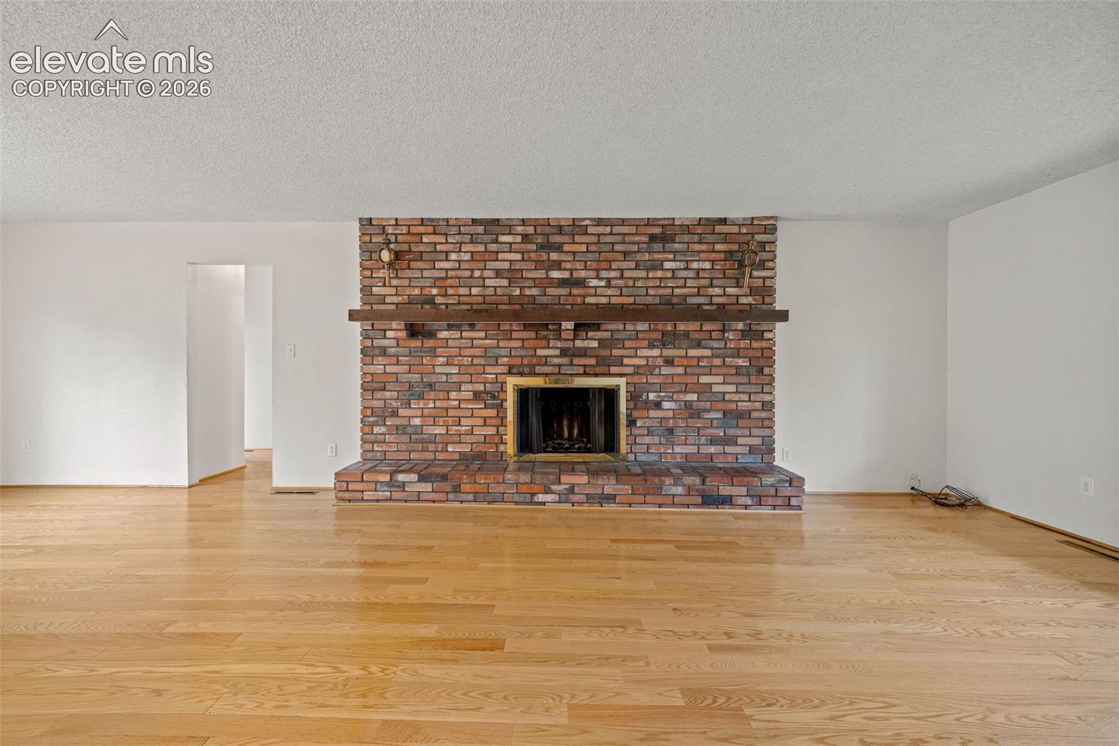 Full-height brick fireplace featuring a wood mantel, brass-finish firebox surround, and a raised brick hearth, complemented by wood-finish flooring