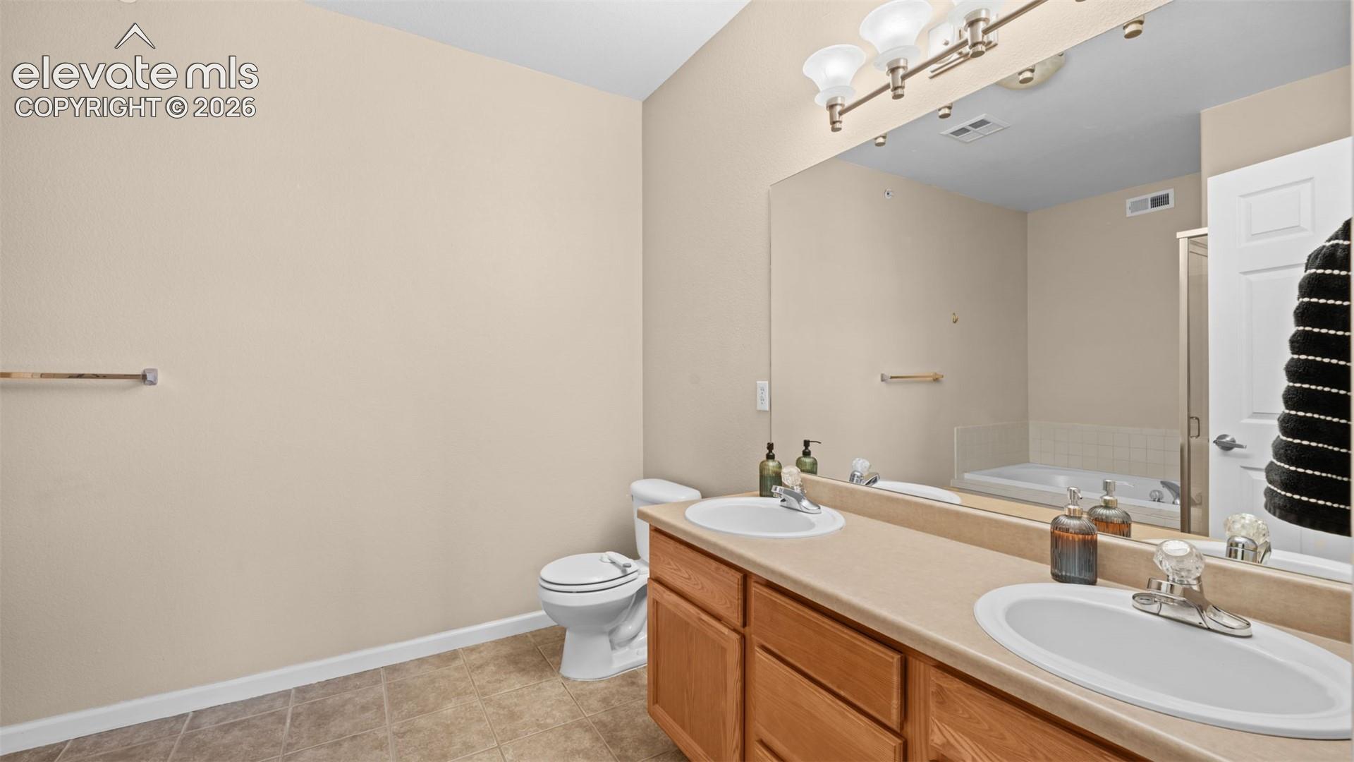Bathroom featuring a dual vanity with oak-finish cabinetry, integrated sinks, a large wall-mounted mirror, and a toilet