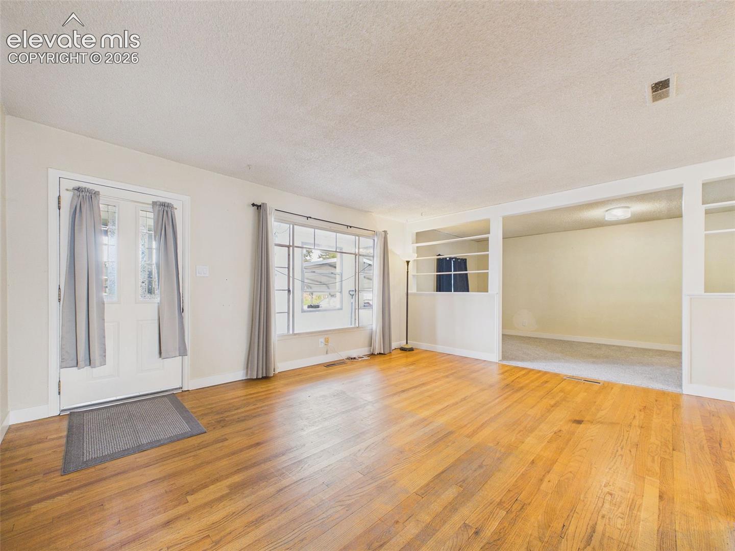 Bright and spacious living room with hardwood flooring, natural light, and built-in shelving separating the adjoining living area.