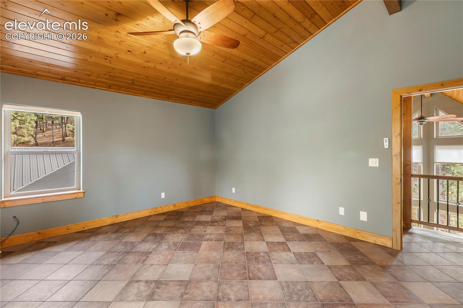 Vaulted wood-plank ceiling featuring a central paddle fan, tile flooring, and natural wood trim throughout